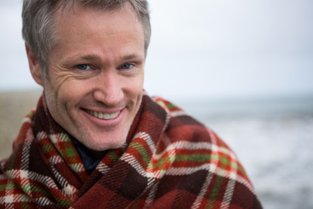 Portrait of smiling man wrapped in shawl at beach
