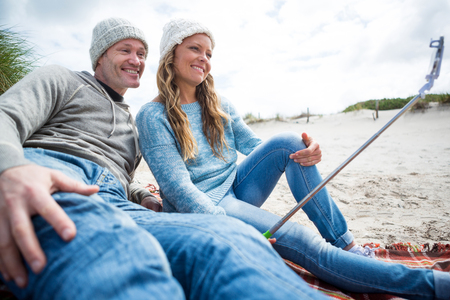 Happy couple taking a selfie from selfie stick at beachの写真素材