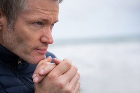 Close-up of thoughtful man with hands clasped at the beachの写真素材