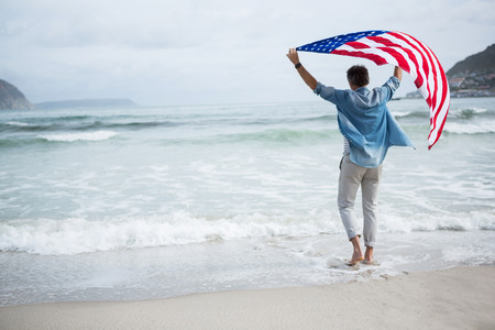 Rear view of man holding american flag on beach during winterの写真素材