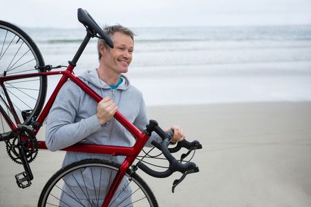 Happy man carrying bicycle on beach during winterの写真素材