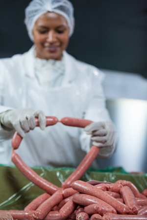 Female butcher processing sausages at meat factoryの写真素材