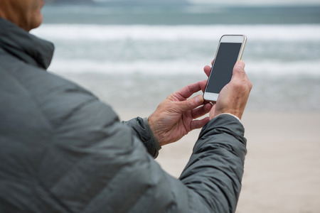 Man using mobile phone on beach during winterの写真素材