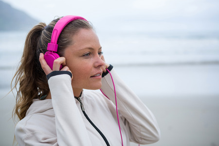 Beautiful woman listening music on headphones at beach during winter