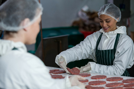 Female butchers processing hamburger patty at meat factoryの写真素材