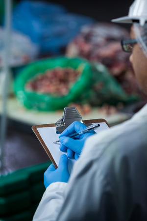 Technicians maintaining records on clipboard at meat factoryの写真素材