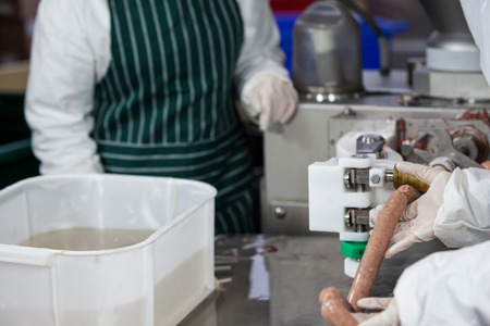 Mid section of butchers processing sausages at meat factoryの写真素材