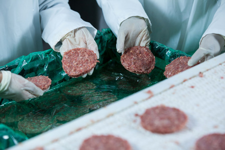 Close-up of butchers processing hamburger patty at meat factoryの写真素材