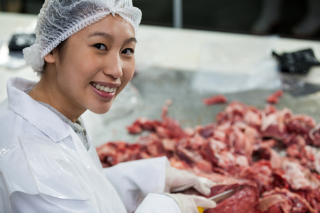 Portrait of female butcher cutting meat at meat factoryの写真素材