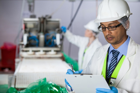 Technician writing on clipboard at meat factoryの写真素材