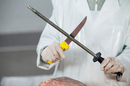 Mid section of butcher sharpening his knife at meat factory