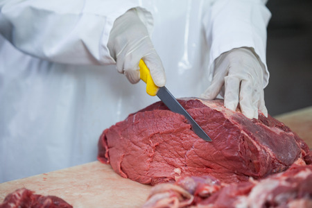 Close-up of butcher cutting meat at meat factory