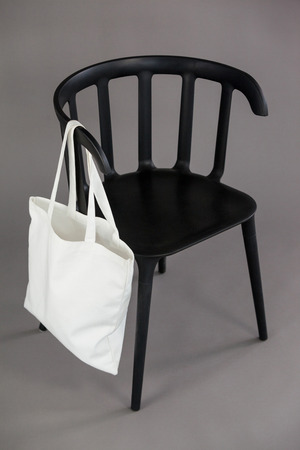 White shopping bag hanging on black chair against grey backgroundの写真素材