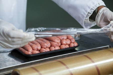 Close-up of butcher packing raw sausages at meat factoryの写真素材