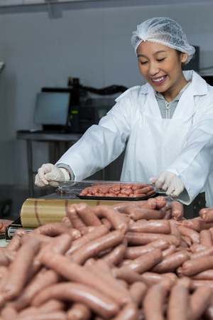 Female butcher packing raw sausages at meat factoryの写真素材