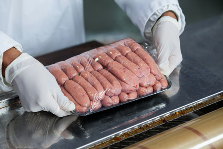 Close-up of butcher packing raw sausages at meat factoryの写真素材