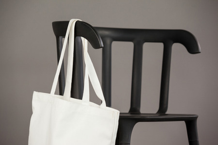 White shopping bag hanging on black chair against grey backgroundの写真素材