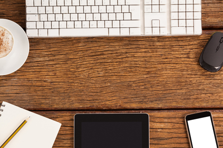 Computer keyboard, mouse, digital tablet and smartphone with coffee cup on wooden tableの写真素材