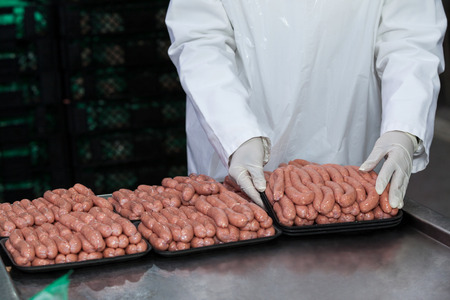 Mid section of butcher packing raw sausages at meat factoryの写真素材