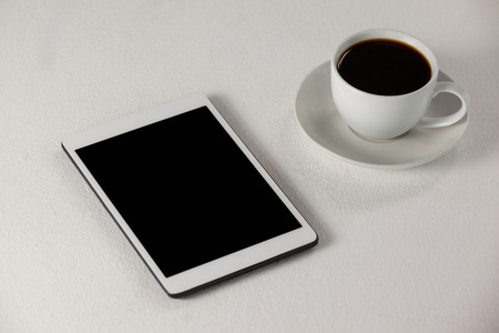 Digital tablet and cup of coffee against white backgroundの写真素材