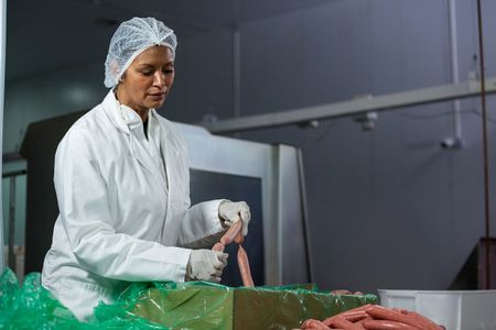 Female butcher processing sausages at meat factoryの写真素材