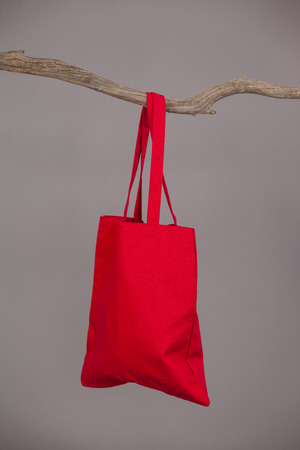 Red bag hanging on a tree branch against grey backgroundの写真素材
