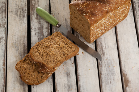 Sliced bread loaf with knife on wooden background