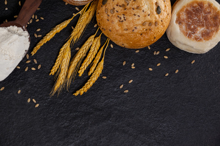 Bread loaves with flour and wheat grains on black surface