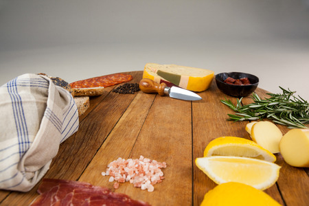 Cheese, ham and bread with various ingredients on chopping board against white background