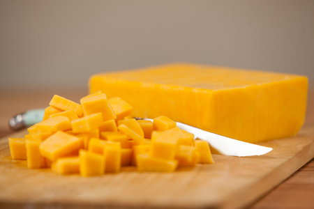 Cubes of cheese with knife on wooden boardの写真素材