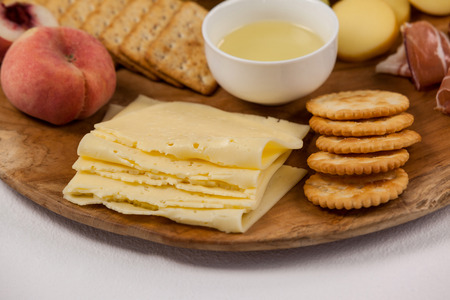 Close-up of different types of cheese, crispy biscuits, fruits and sauce on wooden board against...
