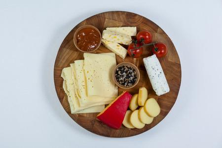 Different types of cheese, tomatoes and bowl of jam on wooden boardの写真素材