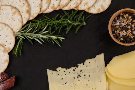 Close-up of cheese, rosemary, sausages, spices, and potatoes on slate boardの写真素材