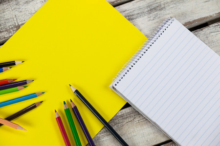 Yellow placard, color pencils and notepad on wooden background