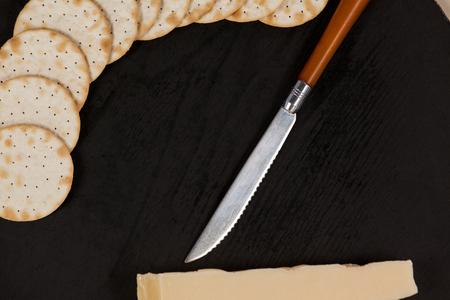 Close-up of slice of cheese with crispy biscuits and knife on chopping boardの写真素材