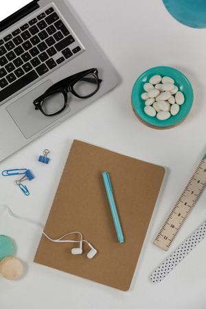 Laptop, spectacles, earphones, macaroons and office desk tops on white backgroundの写真素材