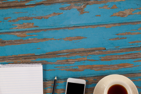 Notepad, pencil, smartphone and cup of tea on wooden plank