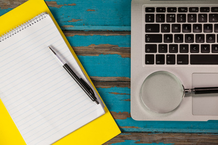 Laptop, magnifying glass, notepad and pen on wooden backgroundの写真素材