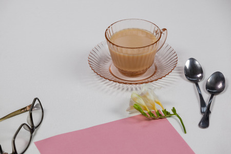 Cup of tea, spoons, blank page, spectacles, paper balls and flower on white backgroundの写真素材