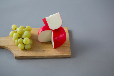 Gouda cheese with grapes on chopping board against grey backgroundの写真素材