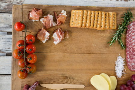 Roquefort cheese, biscuits and ham with various ingredients on chopping board against white backgroundの写真素材