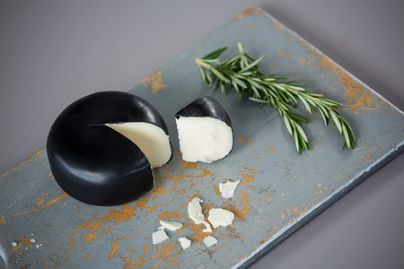 Gouda cheese with rosemary leaves on chopping board against grey backgroundの写真素材