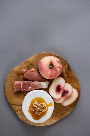 Peach with meat and brie cheese on wooden board against grey backgroundの写真素材