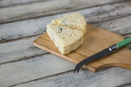 Slices of cheese with knife on wooden boardの写真素材