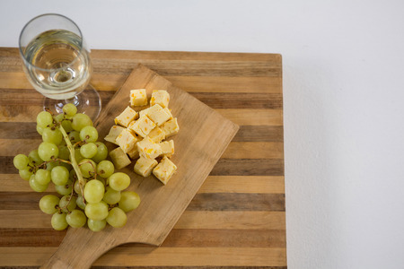 Cubes of cheese with grapes and wine glass on wooden boardの写真素材