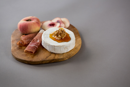 Peach with meat and brie cheese on wooden board against grey backgroundの写真素材
