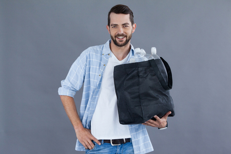 Portrait of a man holding a bag full of plastic bottles against grey backgroundの写真素材
