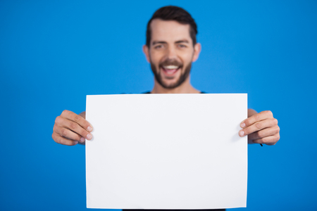 Portrait of a handsome man holding a blank placard against blue backgroundの写真素材