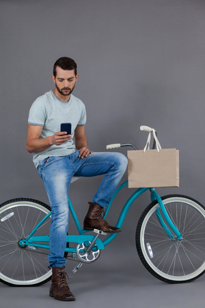 Man sitting on a bicycle and using mobile phone against grey backgroundの写真素材