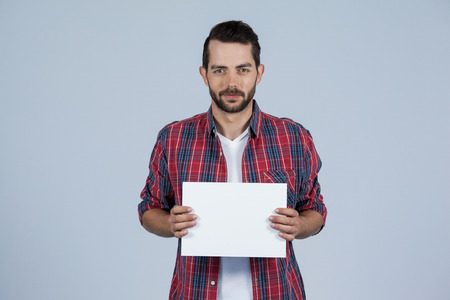Portrait of man holding a blank placard against grey backgroundの写真素材